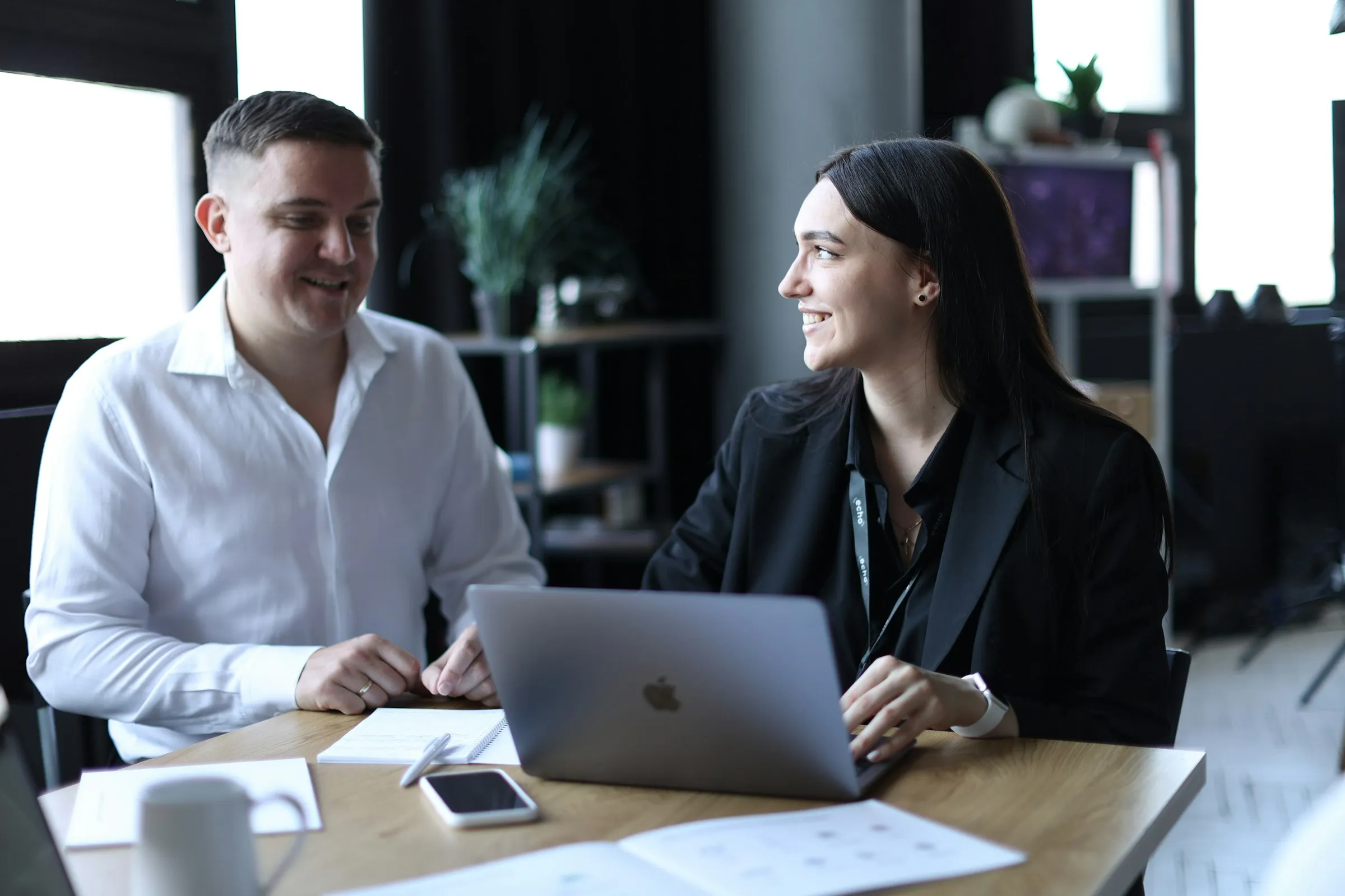 Two colleagues talking across a desk with a laptop