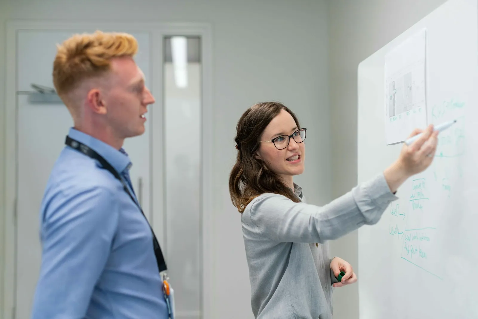 Colleague explaining a plan on a whiteboard to a coworker