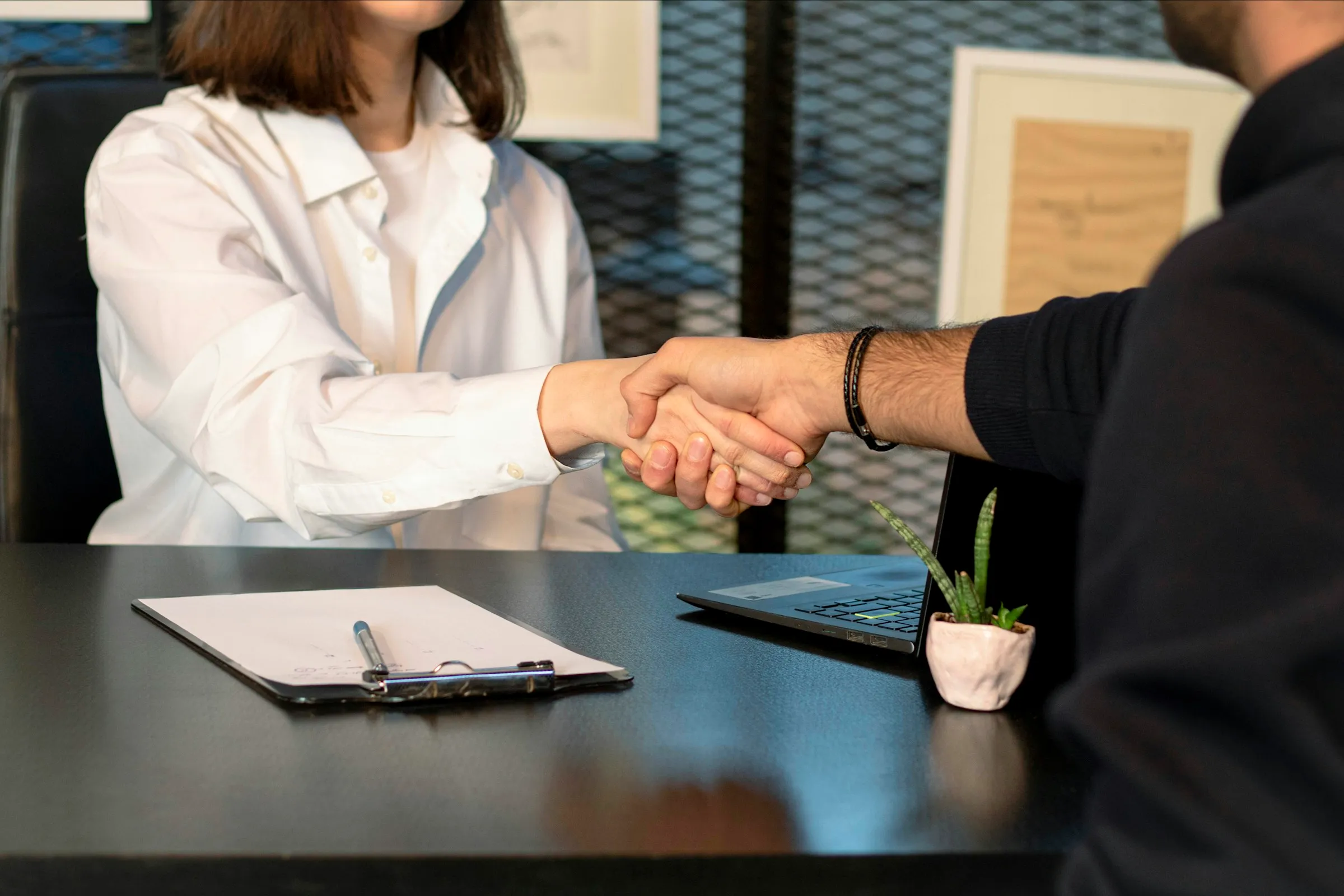 Handshake across a desk with a clipboard and documents