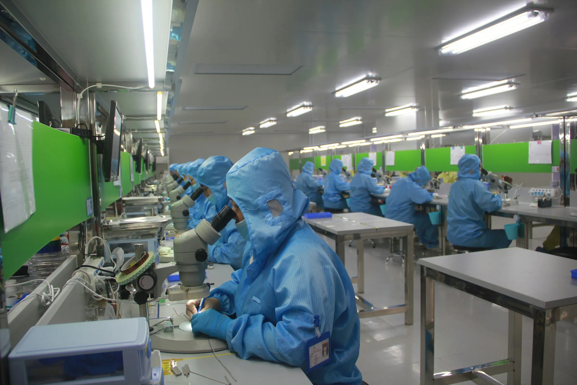 Technicians in cleanroom suits inspecting parts under microscopes